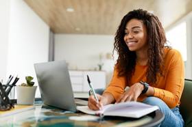 Lady looking at laptop, smiling and writing notes