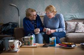 Two ladies sitting on a couch drinking tea and chatting