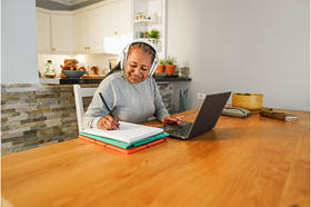 Lady with headphones and laptop taking notes on a notepad